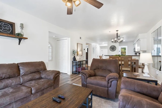 living room featuring ceiling fan with notable chandelier and light wood-type flooring