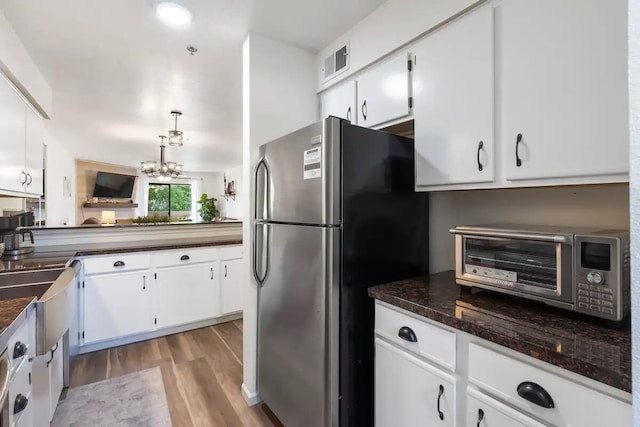 kitchen featuring light wood-type flooring, white cabinets, stainless steel fridge, a notable chandelier, and hanging light fixtures