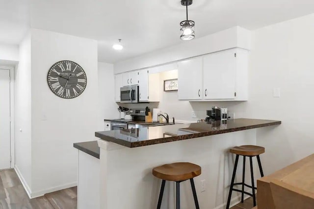 kitchen featuring light wood-type flooring, sink, kitchen peninsula, white cabinets, and appliances with stainless steel finishes