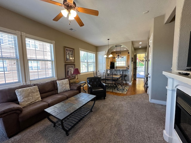 carpeted living room with ceiling fan with notable chandelier and a textured ceiling