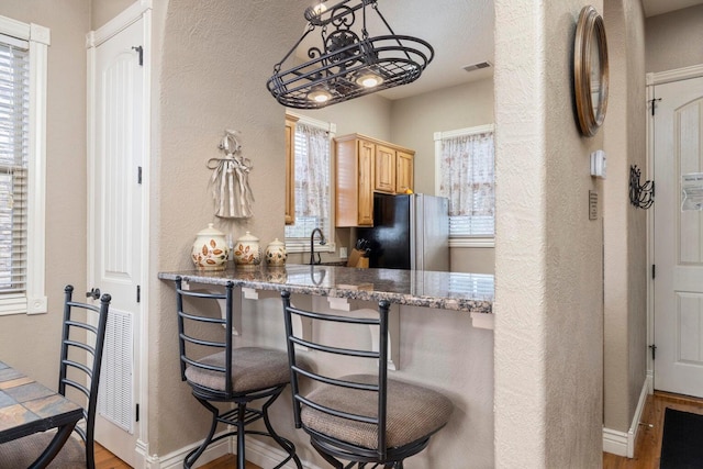 kitchen featuring a kitchen bar, light brown cabinetry, stainless steel fridge, kitchen peninsula, and dark stone counters