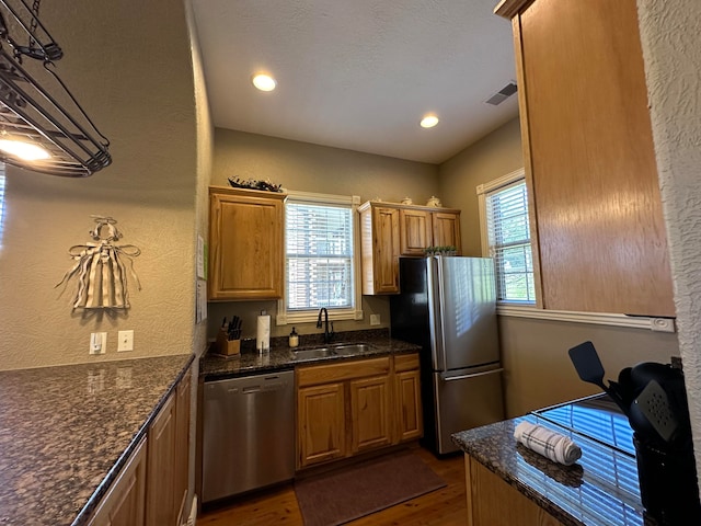 kitchen featuring dark stone countertops, decorative light fixtures, sink, dark hardwood / wood-style floors, and appliances with stainless steel finishes