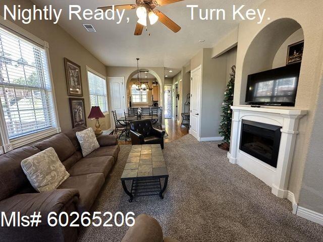 carpeted living room with ceiling fan with notable chandelier