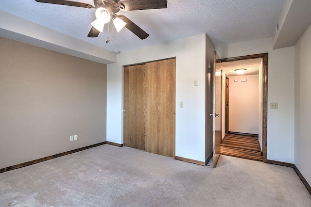 unfurnished bedroom with light colored carpet, ceiling fan, a closet, and a textured ceiling