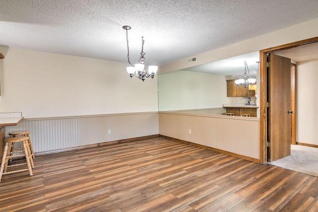 unfurnished dining area featuring wood-type flooring, sink, a notable chandelier, and a textured ceiling