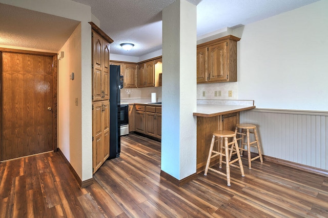 kitchen featuring wooden walls, dark hardwood / wood-style floors, kitchen peninsula, a kitchen bar, and a textured ceiling