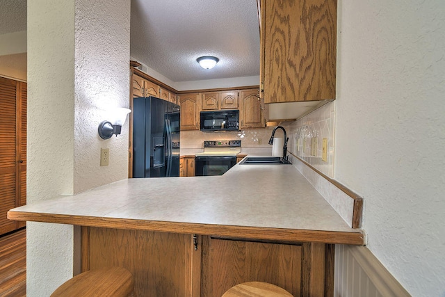 kitchen featuring sink, kitchen peninsula, backsplash, black appliances, and hardwood / wood-style flooring