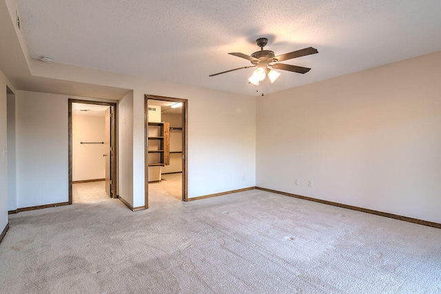 unfurnished bedroom featuring ceiling fan, a textured ceiling, a closet, a spacious closet, and light carpet