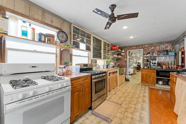 kitchen featuring ceiling fan, gas range gas stove, brick wall, stainless steel gas range, and black microwave