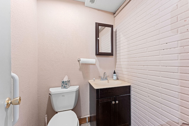 bathroom with vanity, toilet, and brick wall