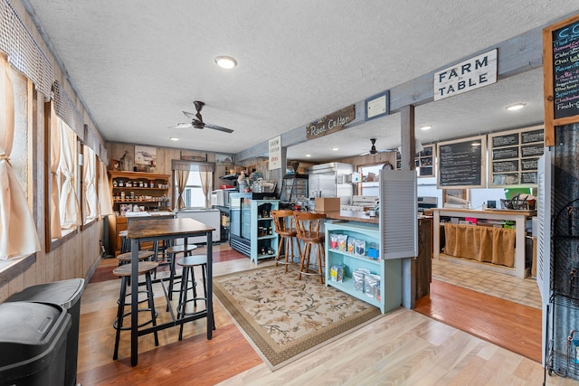 dining room with ceiling fan, a textured ceiling, light wood-type flooring, and wooden walls