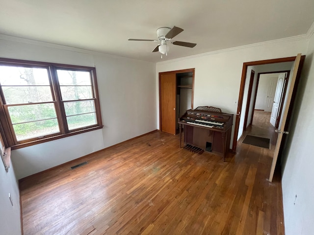 unfurnished bedroom with ceiling fan, ornamental molding, a closet, and dark wood-type flooring