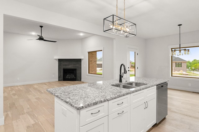 kitchen with pendant lighting, an island with sink, sink, stainless steel dishwasher, and white cabinetry