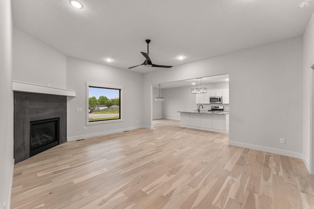 unfurnished living room with a tiled fireplace, ceiling fan, sink, and light hardwood / wood-style floors