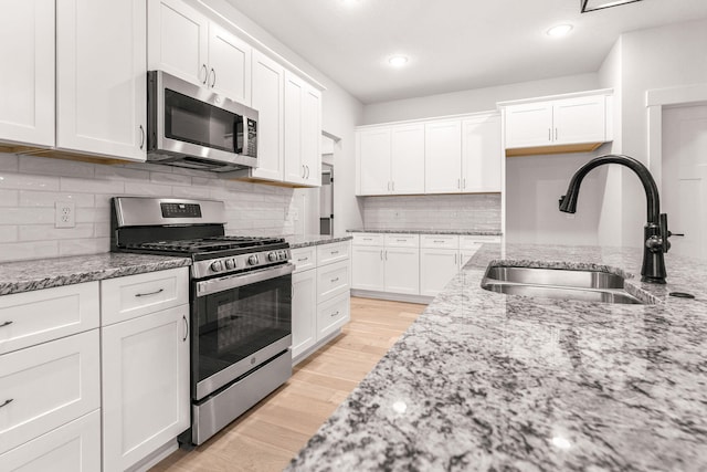 kitchen with light wood-type flooring, sink, stainless steel appliances, light stone countertops, and white cabinetry