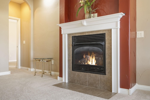 interior details featuring arched walkways, carpet, a tile fireplace, and baseboards