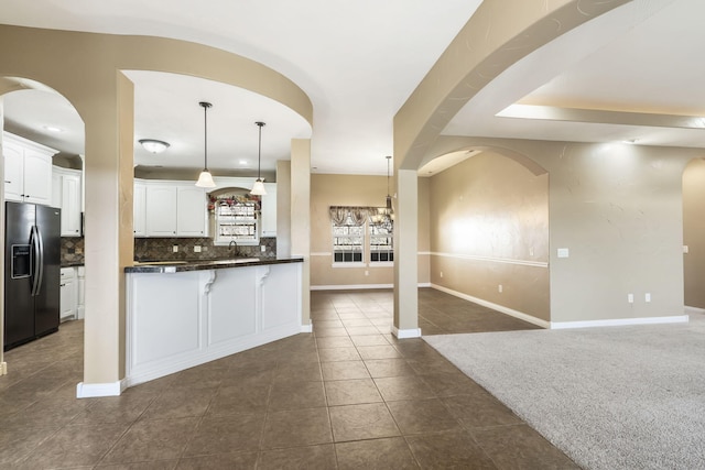 kitchen featuring dark countertops, open floor plan, black refrigerator with ice dispenser, a kitchen bar, and white cabinetry