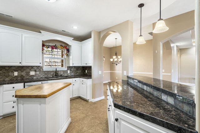 kitchen featuring light tile patterned floors, arched walkways, decorative backsplash, butcher block countertops, and a sink