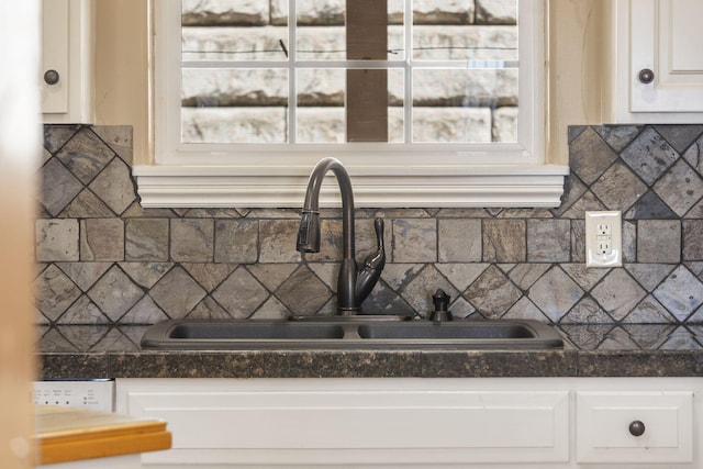 kitchen with dark countertops, white cabinetry, decorative backsplash, and a sink