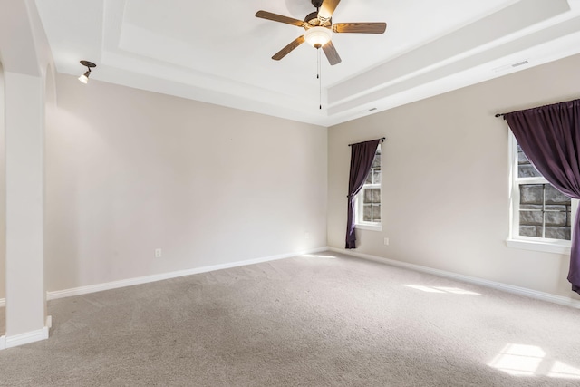 spare room featuring carpet floors, a tray ceiling, visible vents, a ceiling fan, and baseboards