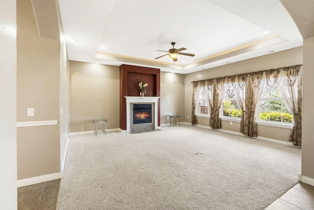 unfurnished living room featuring carpet floors, a raised ceiling, a fireplace with flush hearth, ceiling fan, and baseboards