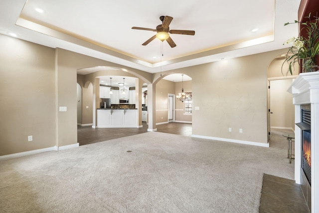 unfurnished living room featuring arched walkways, a lit fireplace, a tray ceiling, and carpet flooring