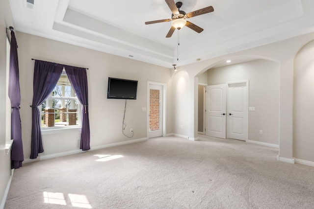 interior space featuring a tray ceiling, arched walkways, carpet, ceiling fan, and baseboards