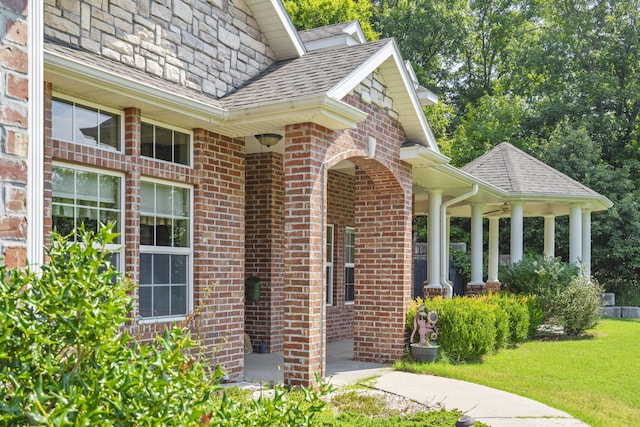 view of exterior entry with a yard, a shingled roof, and brick siding