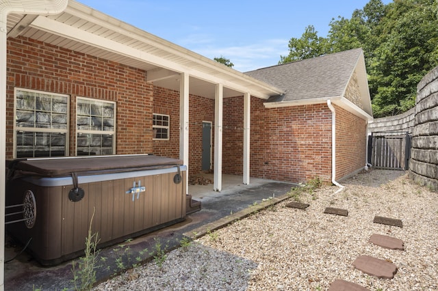 view of side of property featuring a hot tub, fence, roof with shingles, and brick siding