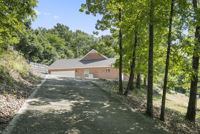 view of side of property featuring brick siding, driveway, an attached garage, and fence