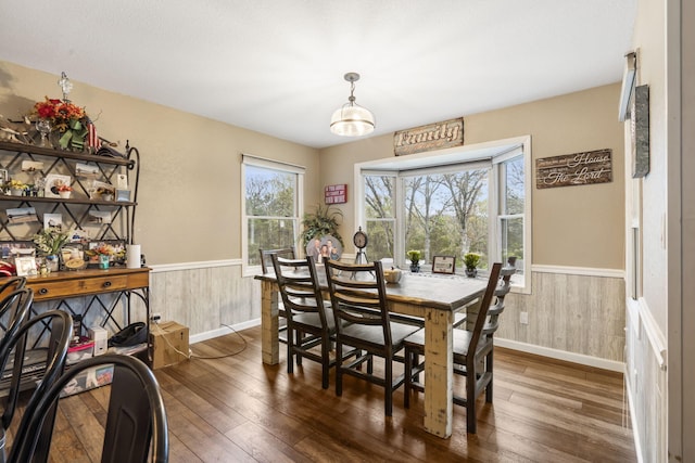 dining area featuring baseboards, a wainscoted wall, wood walls, and dark wood-type flooring