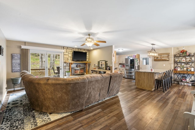 living room with ceiling fan, a stone fireplace, and dark hardwood / wood-style floors