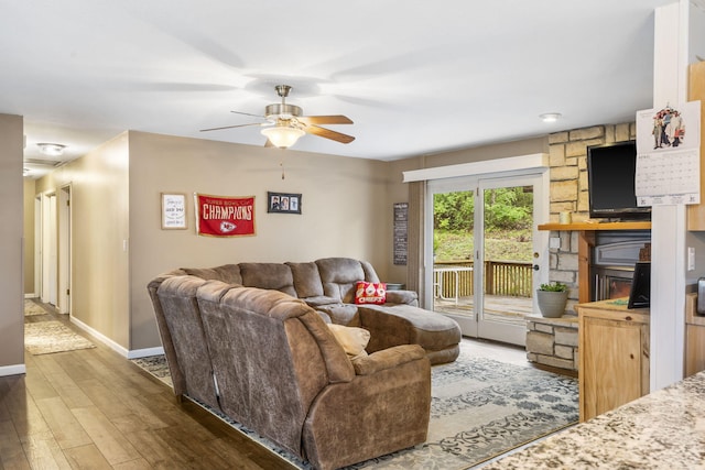 living room featuring ceiling fan, a stone fireplace, and dark hardwood / wood-style floors