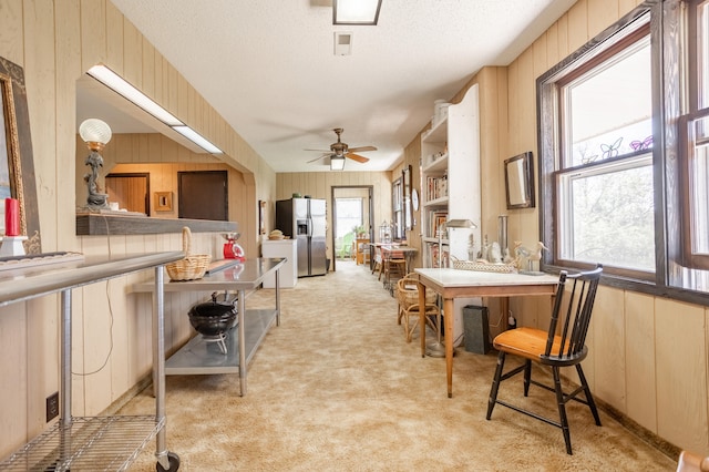 carpeted dining area with ceiling fan, a textured ceiling, and wooden walls