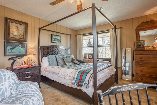 carpeted bedroom featuring wooden walls, a textured ceiling, and ceiling fan