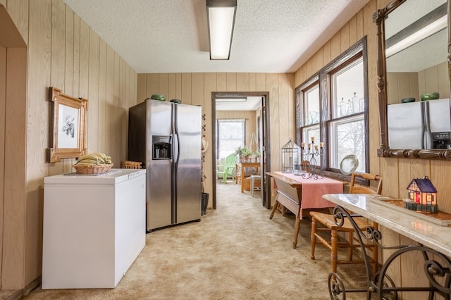 kitchen featuring light carpet, wood walls, and stainless steel fridge with ice dispenser