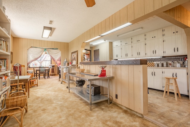 kitchen featuring white cabinetry, a breakfast bar area, light carpet, kitchen peninsula, and a textured ceiling