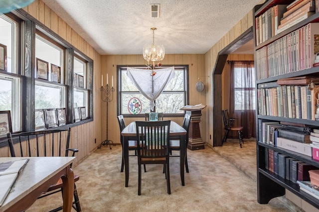 carpeted dining room featuring a notable chandelier, wooden walls, and a textured ceiling