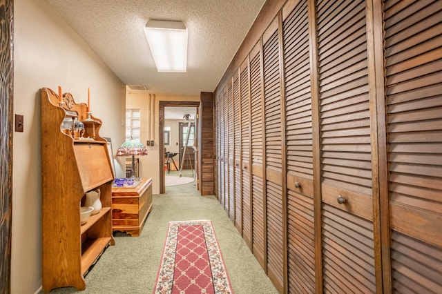 hall featuring light colored carpet and a textured ceiling