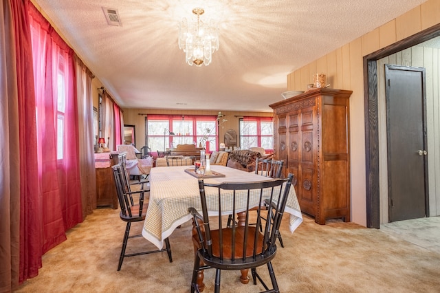 dining area featuring light carpet, an inviting chandelier, and a textured ceiling