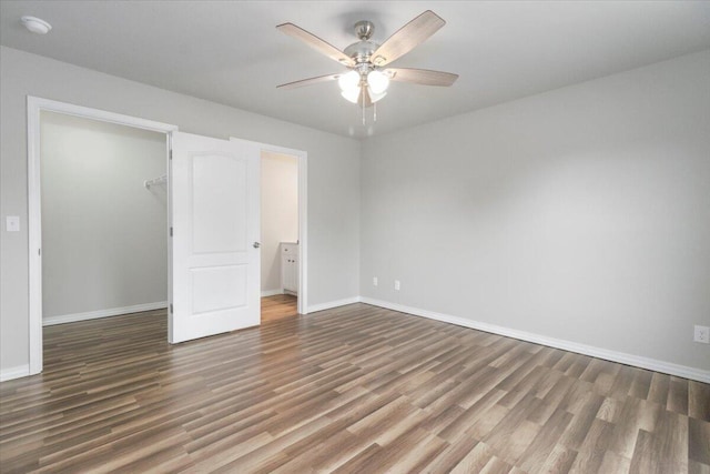 unfurnished bedroom with a spacious closet, a closet, dark hardwood / wood-style flooring, and ceiling fan