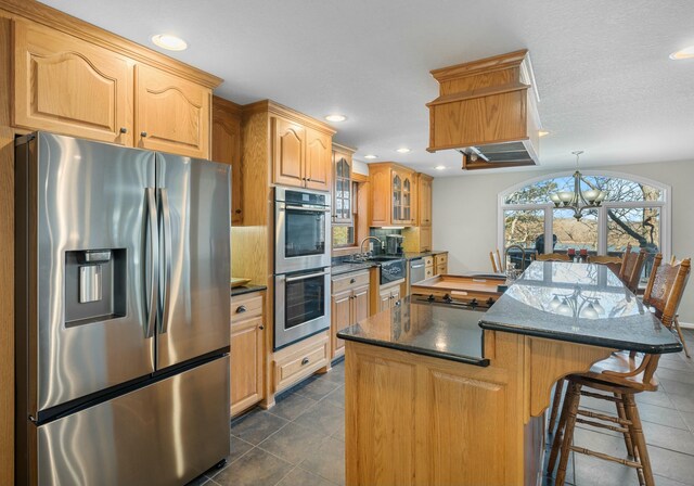 kitchen with a kitchen island, a breakfast bar area, dark tile patterned flooring, a notable chandelier, and stainless steel appliances