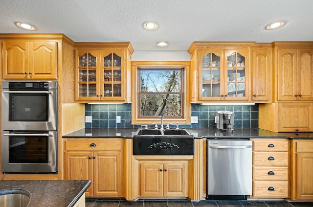 kitchen featuring stainless steel appliances, sink, decorative backsplash, and dark stone counters