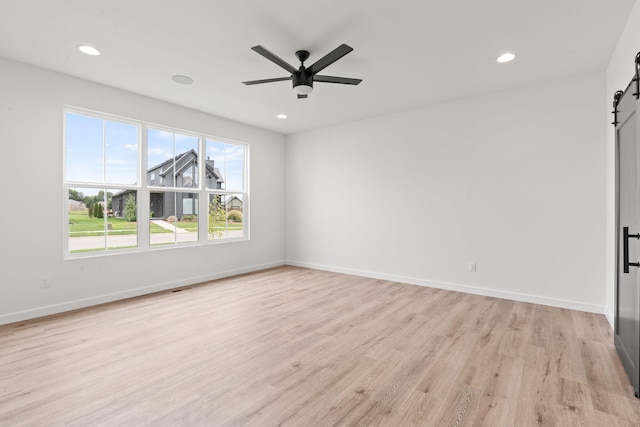 empty room featuring ceiling fan, a barn door, and light hardwood / wood-style flooring