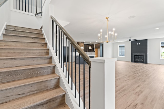 stairs with ceiling fan with notable chandelier, a large fireplace, and hardwood / wood-style floors