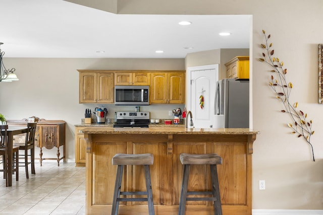 106 Willowbrooke, Branson, MO 65616 - kitchen with light stone counters, brown cabinetry, light tile patterned flooring, stainless steel appliances, and a kitchen bar
