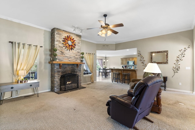 carpeted living room featuring a stone fireplace, ornamental molding, ceiling fan with notable chandelier, and track lighting