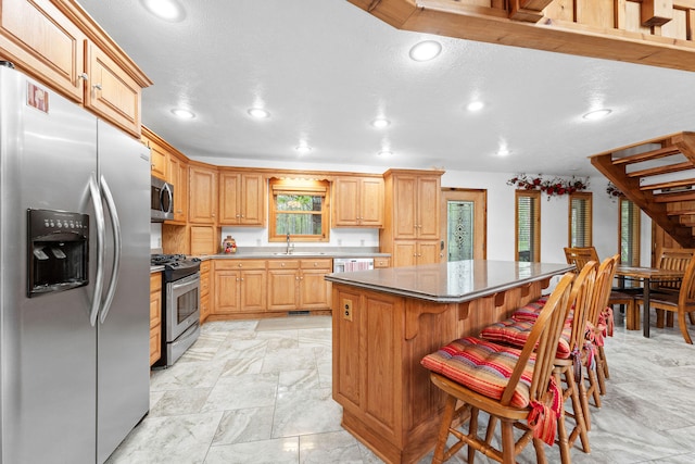 kitchen featuring a kitchen island, a kitchen breakfast bar, light brown cabinets, sink, and stainless steel appliances