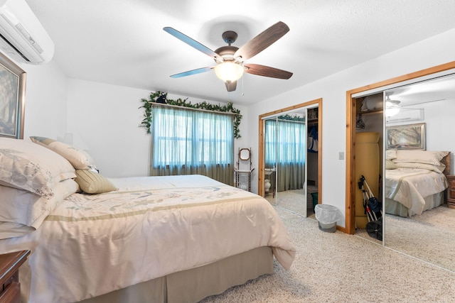 bedroom featuring ceiling fan, two closets, a wall mounted air conditioner, and light carpet