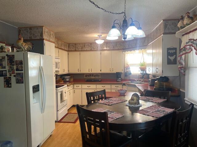 kitchen with light hardwood / wood-style floors, white appliances, a notable chandelier, hanging light fixtures, and white cabinets